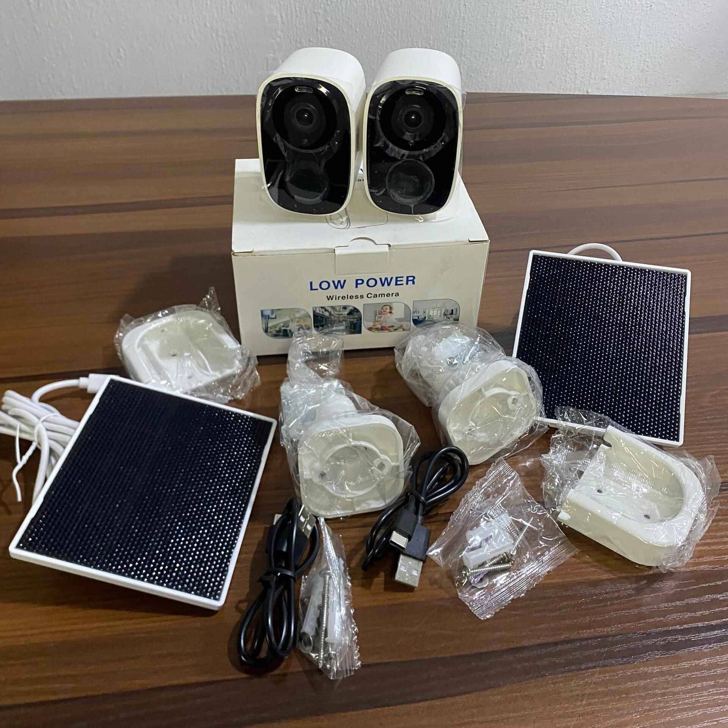 Set of security cameras and accessories on a wooden surface with a white wall background.